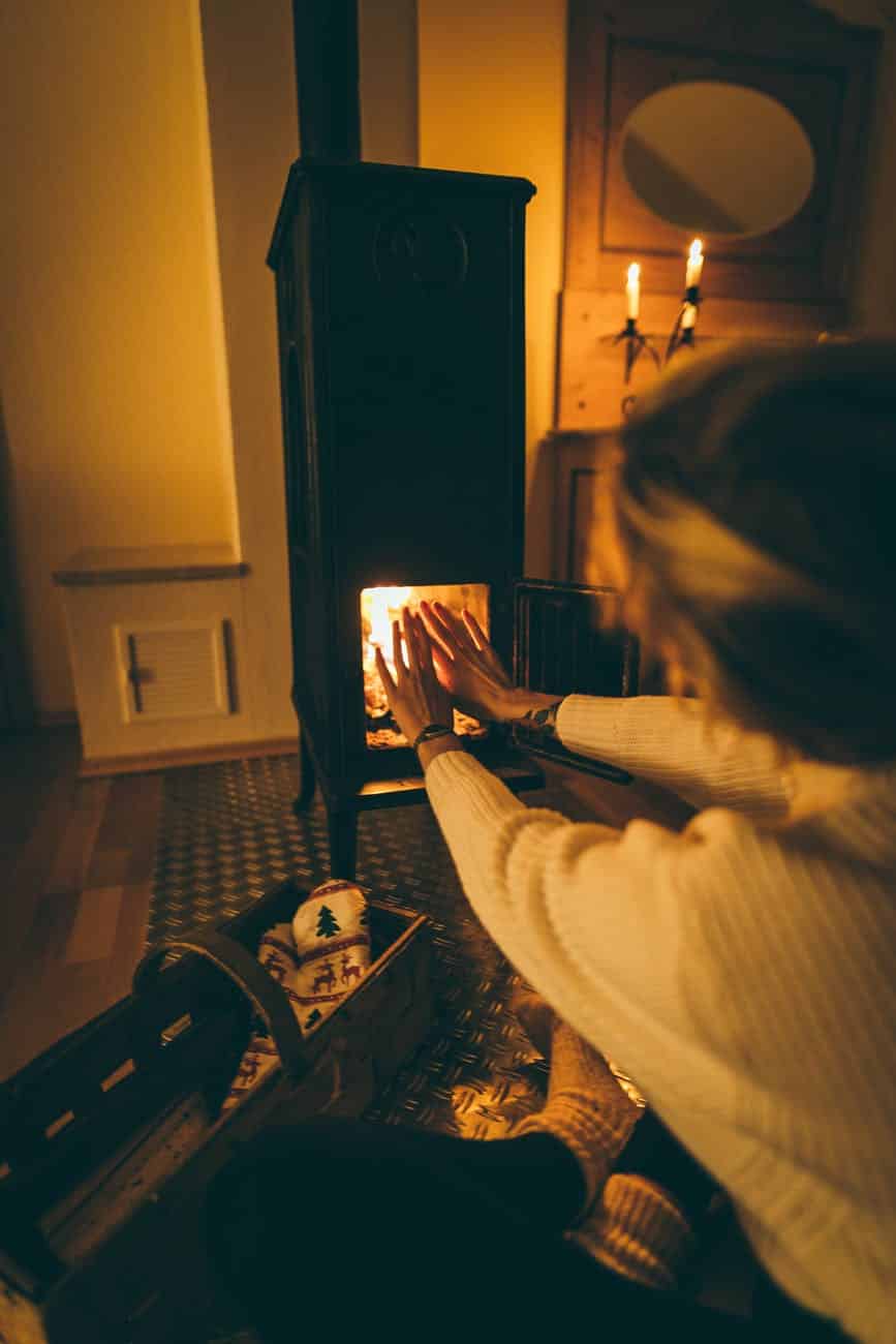 woman wearing white long sleeved try to get heat at fireplace