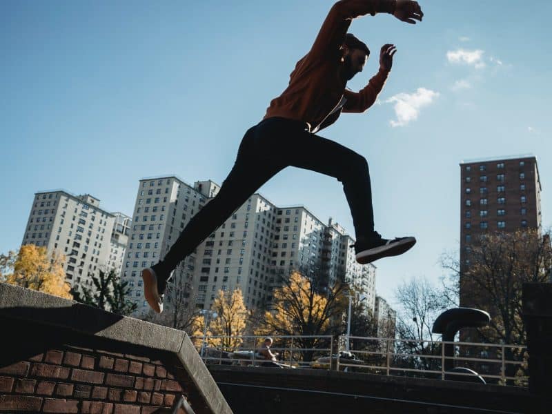fit man jumping from brick parapet in urban city