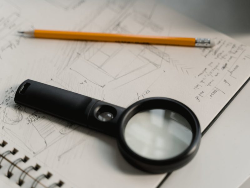 black magnifying glass beside yellow pencil